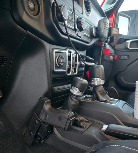 Reviewer's Universal Accessory Mount installed in a Jeep, holding a black handgun holster next to the center console.