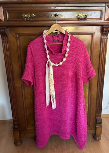 Reviewer's fuchsia crinkled dress with custom shortened sleeves, hanging on a hanger in front of a wooden dresser.