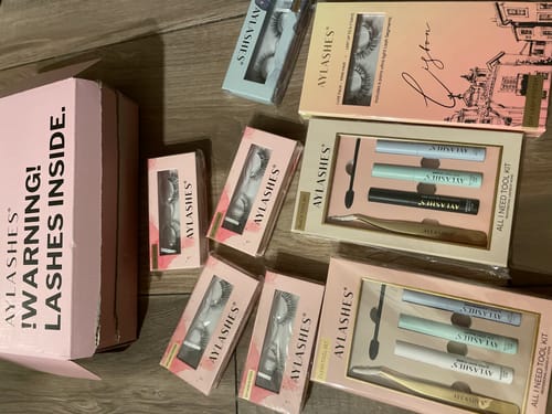Ein Kunde zeigt seine AYLASHES Bundle Builder-Bestellung mit verschiedenen Wimpernsets und Werkzeugkästen, die auf einer Oberfläche ausgelegt sind.