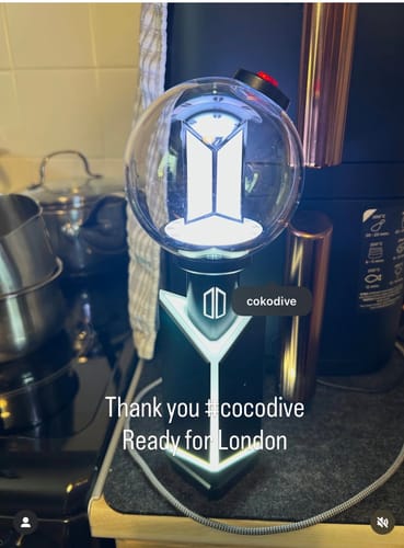 Customer's BTS Official Light Stick Ver.4, lit up and sitting on its black cradle in their home.