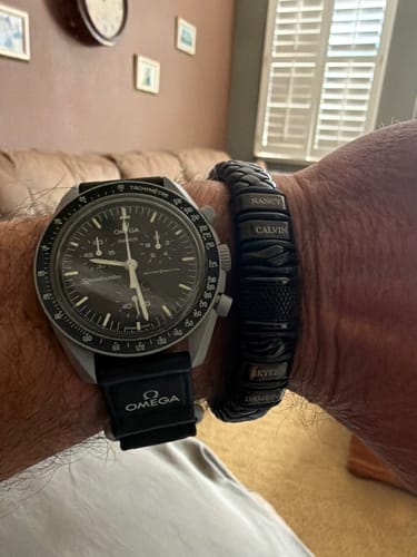 Customer's wrist showing the personalized black bracelet worn next to a watch.
