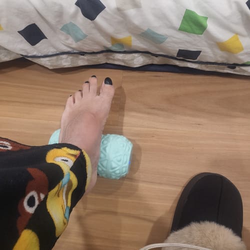 Customer massaging their foot with the light blue Vibit ROLL on a wooden floor.