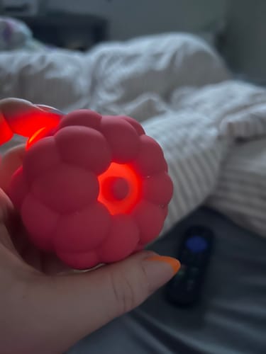 Close-up of a reviewer holding the pink Berri massager while it glows with a red light.
