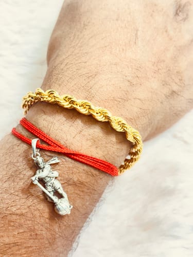 Customer's wrist wearing the thick Golden Rope Bracelet next to a red string bracelet with a silver pendant.