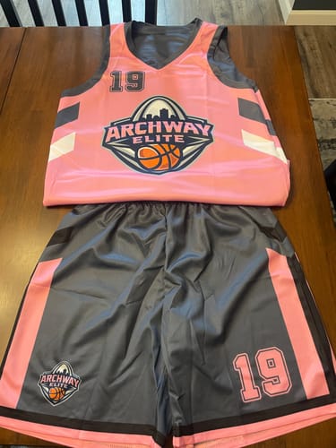 Customer's custom pink and gray basketball jersey and shorts with the 'Archway Elite' logo and number 19 laid out on a table.