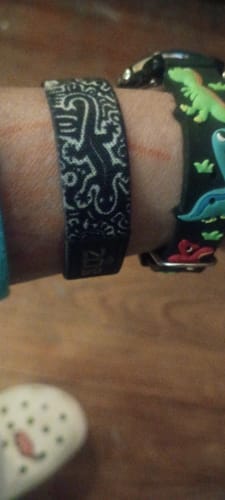 Close-up of a customer's wrist wearing the black Emerging Light Collection bracelet with a white axolotl design.
