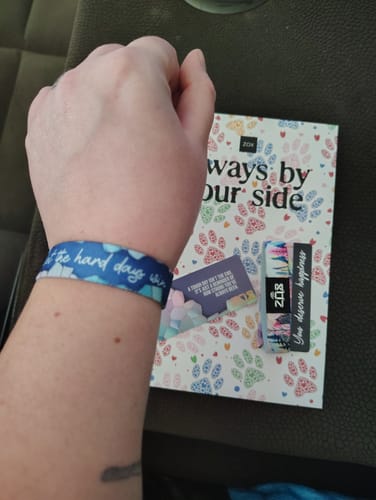 Reviewer wearing the blue Don't Let the Hard Days Win Bracelet on their wrist, with the product packaging nearby.