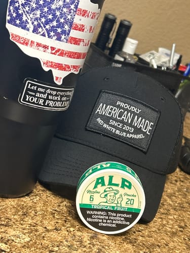 Customer's can of Tropical Fruit Nicotine Pouches next to an American-themed hat and tumbler.