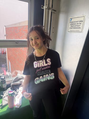 Reviewer smiling while wearing the black 'Girls Just Wanna Make Gains' loose crop top indoors.