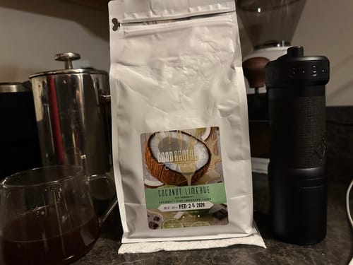 Customer's bag of Coconut Limeade coffee on a counter with a coffee grinder and a glass of brewed coffee.