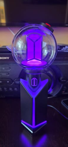 Customer's BTS Official Light Stick Ver. 4 glowing with purple light while placed in its cradle on a desk.