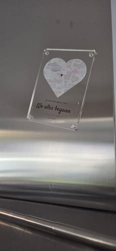Kunde zeigt den 'Unser Ereignis' Acryl-Magneten mit herzförmiger Karte, der an einer Edelstahloberfläche befestigt ist.