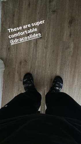 Reviewer shows a first-person view of their patterned black slides on a wooden floor.