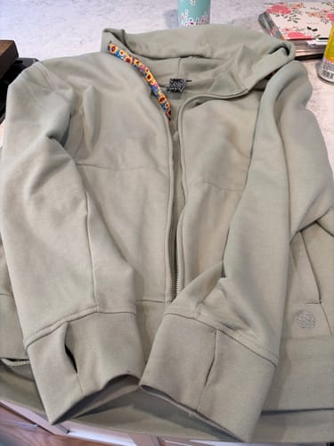 Reviewer's StringSwap Zip Hoodie in Matcha Green laid flat and unzipped, showing the thumbholes in the cuffs.