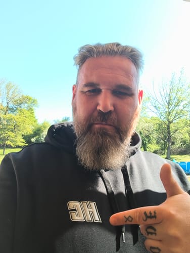 Client portant le Hoodie HC Argenté noir en extérieur, pointant le logo sur la poitrine.