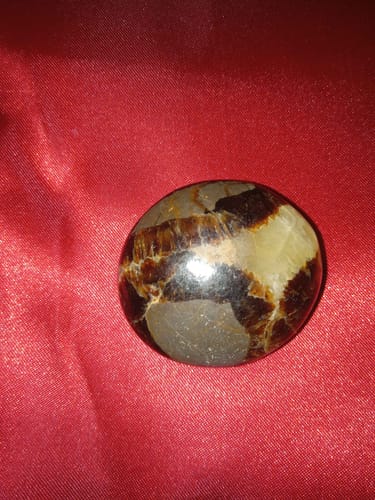 Customer's piece of Septarian crystal, a polished palm stone with brown and yellow patterns on a red cloth.