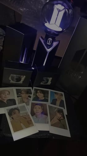 Reviewer's lit BTS Official Light Stick Ver.4 in its cradle, displayed with the product packaging and seven member photocards.