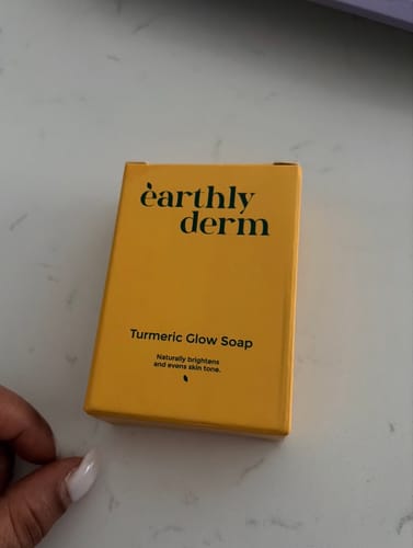 Customer holding the yellow packaging for the Turmeric Fade & Glow Bar on a marble counter.
