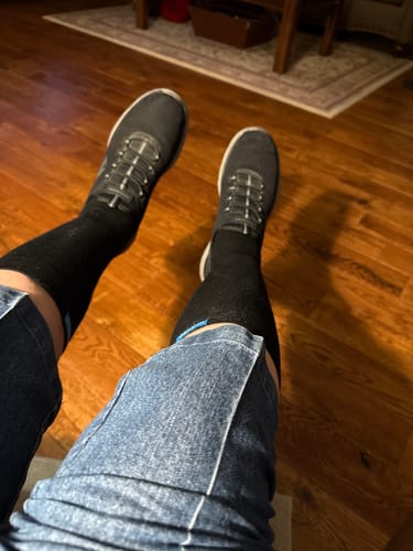 Reviewer relaxing with their legs up, wearing black Performance Eucalyptus Compression Socks with sneakers.