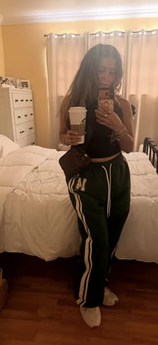 Customer taking a mirror selfie in a bedroom wearing the green W280 Weekend Track Pants.