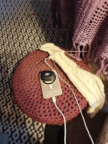 Customer's GoldPower power bank charging an earbud case on a round knitted pouf, next to a knitting project.
