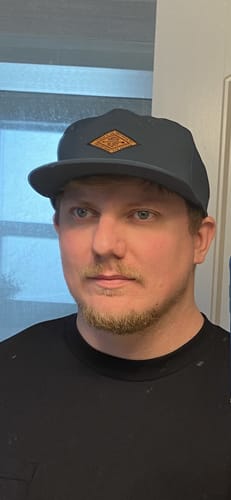 Reviewer wearing the dark Big Flat Bill Unstructured Wicking Hat, showing the front fit and logo.