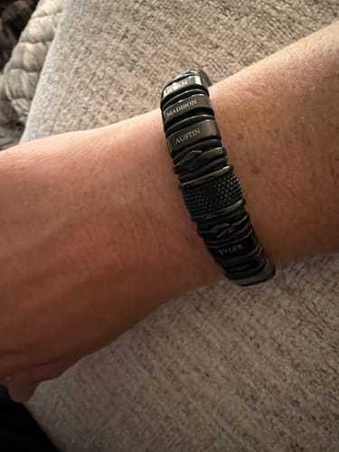 Customer wearing a black bracelet with several personalized name rings on their wrist.