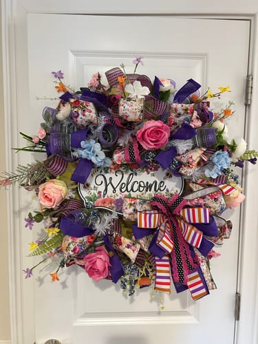 Reviewer's completed, colorful wreath with a "Welcome" sign, made using the white wire work wreath frame and hung on a door.