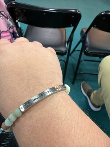 Customer's wrist wearing the beaded bracelet engraved with 'God is within her she will not fail'.