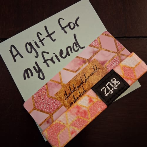 Customer's pink 'She Believed She Could Bracelet' on its backing card next to a note reading 'A gift for my friend'.