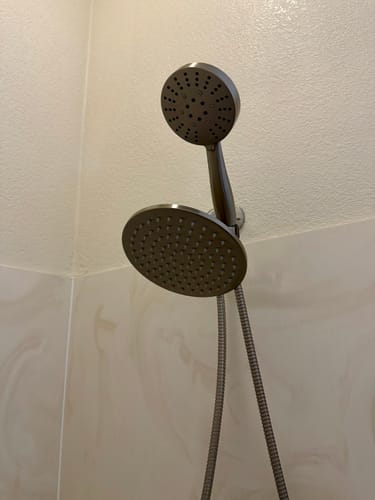 Close-up of the customer's brushed nickel Dual Shower Head Set installed against a tiled shower wall.