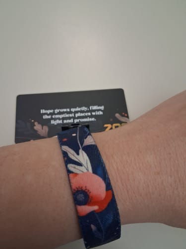 A customer wearing the Fields of Hope Bracelet on their wrist, showing the bright poppy design on the dark blue fabric.