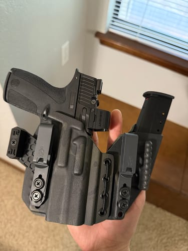 Customer holding a multi-cam black AXIS ELITE sidecar-style holster with a handgun and spare magazine.