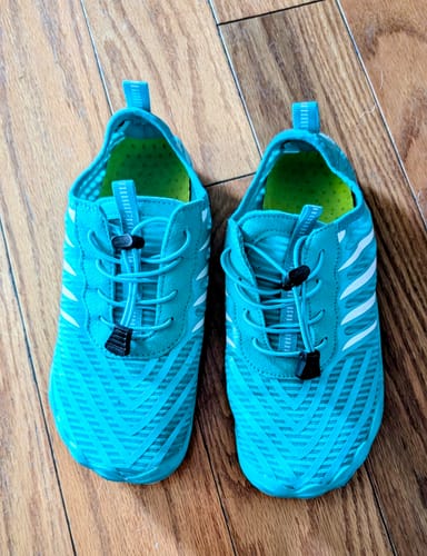 Reviewer's pair of turquoise Lorax Pro barefoot shoes with elastic laces, shown on a wood floor.
