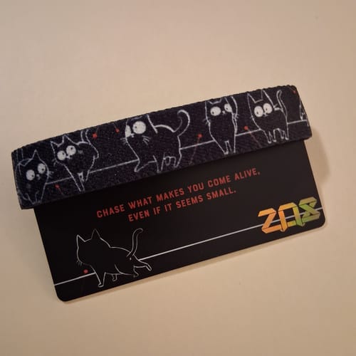 Customer's black Laser Focus Cat Bracelet with a cartoon cat pattern, displayed on its original packaging card.