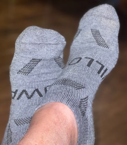Close-up of a reviewer wearing the gray Men's Alpaca Socks with their feet crossed.