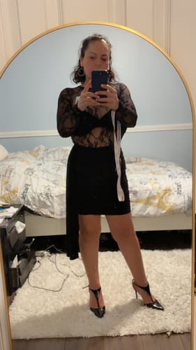 Reviewer in a mirror selfie wearing the black Isadora Lace Sash Mini Dress, showing its sheer lace top and side sash detail.