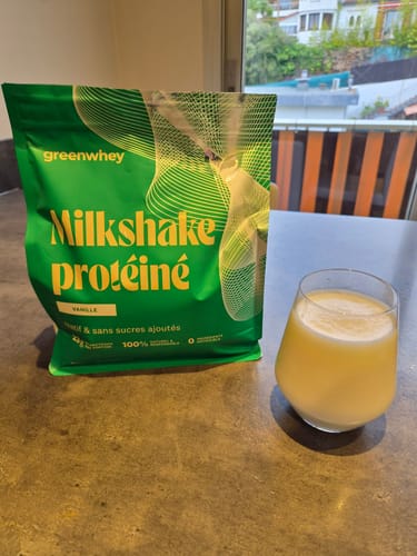 Un client montre son sachet de Milkshake protéiné à la vanille à côté d'un verre de la boisson crémeuse.