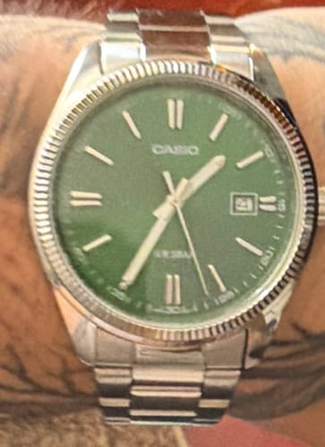 Primer plano del reloj Casio Análogo de un cliente en su muñeca, mostrando la esfera verde y la correa de acero.