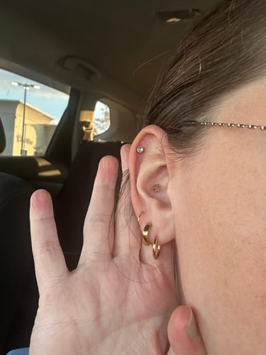 Reviewer in a car showing their ear stack with multiple gold earrings, including the Essential Earrings Extra Small.