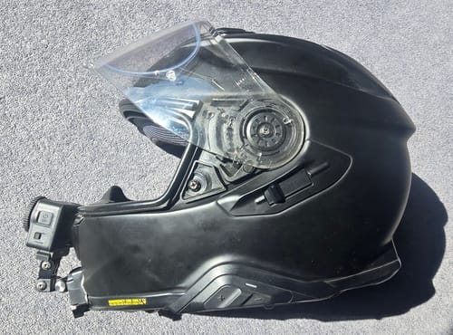 Reviewer's camera mount secured to the chin of a black motorcycle helmet, holding a camera.