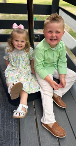 Customer's child wearing the Sunny Days Floral Smocked Bishop Dress, sitting with another child in a green shirt.