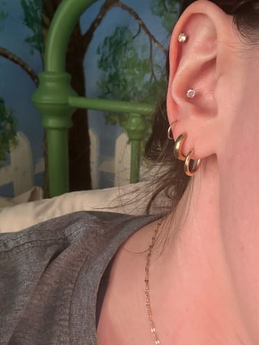 Close-up of the reviewer's ear wearing a stack of gold earrings featuring the Essential Earrings Extra Small.