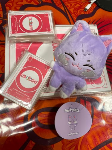 Customer's purple Sandeoki Aniteez plush keyring with a winking face, shown with its tag and other merchandise.