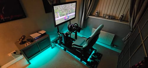 Customer's PRIME Lite Cockpit racing simulator fully assembled in a room, illuminated with cool teal LED lights from underneath.