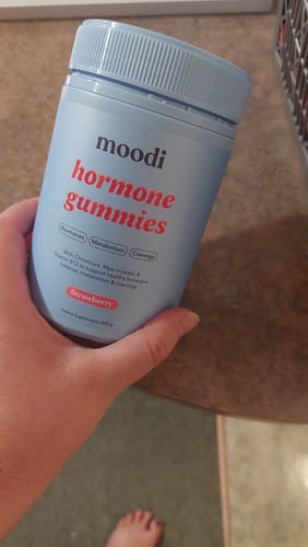 Reviewer holding the light blue container of Strawberry Hormone Gummies.