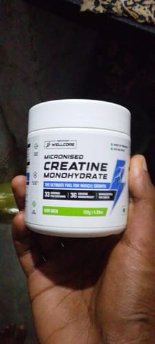 Customer holding a white tub of Wellcore Micronised Creatine Monohydrate in the Kiwi Kick flavor.