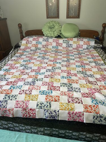Reviewer's finished quilt top from the Brick Prairie Precut Quilt Kit, showing the colorful floral and white block pattern on a bed.