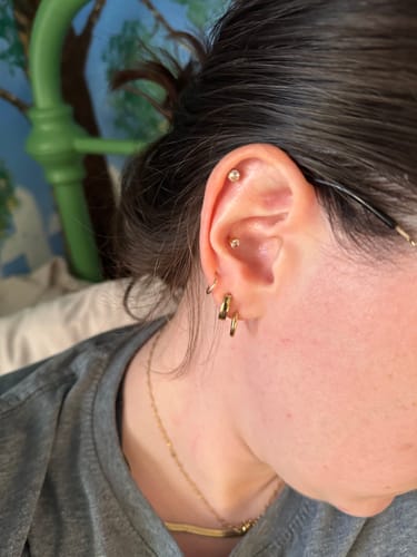 Customer's ear showing a stack of gold earrings, including the small Essential Earrings Extra Small hoops.