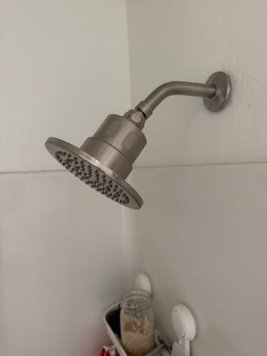 Reviewer's metal Gillian Filtered Shower Head installed in a white tiled shower, showing its brushed finish.